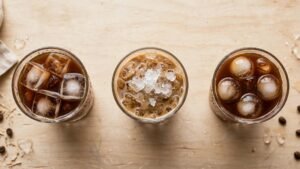 Three glasses of iced coffee with different ice styles on a light wood table.